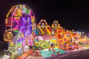 Illuminated Ferris Wheel, Bouncing Castle And Carousel At Night In A Funfair In Vientiane, Laos